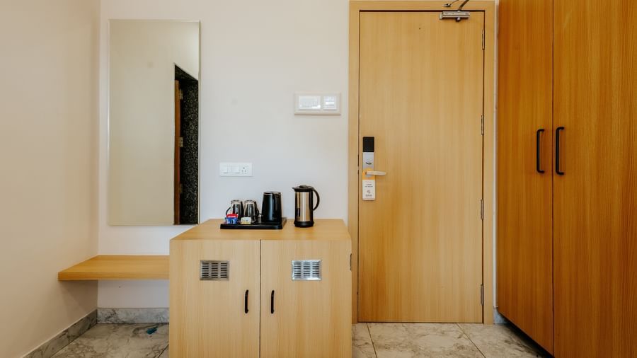 A well-equipped room entry area at Daksh The Grand Gowardhan, Dwarka, with a wardrobe, a dressing table with a long rectangular mirror, and a refreshment station beside it.