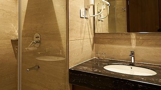 A modern bathroom featuring a glass-enclosed shower, sink, and mirror at The Hamuse Hotel, Kodaikanal.