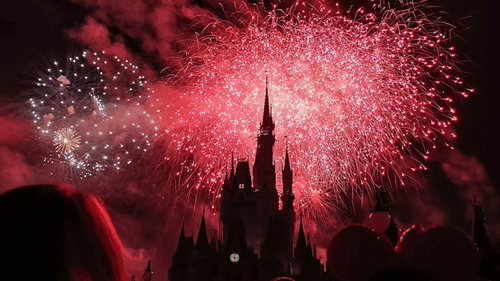 A fireworks display over a castle, with silhouettes of people watching.