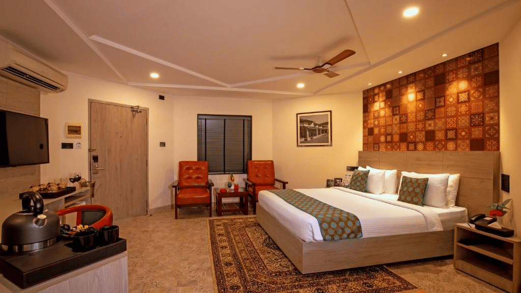 A Cottage by the Sea at MGM Dizzee World featuring a bed, a patterned carpet, 2 leather chairs, an A/C unit and a television.