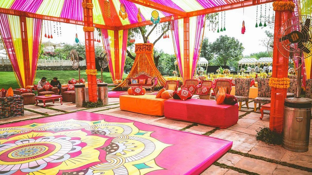 Vibrant Indian wedding decor with colorful tent, patterned floor, and seating, showcasing traditional festive setup.