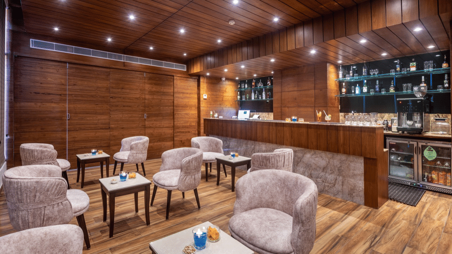 Cozy bar or lounge area with wooden paneling, soft lighting, and cushioned chairs around small tables.