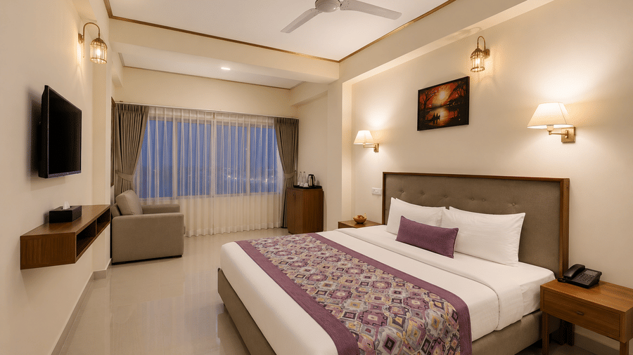 Family Room at Valmere Himalayan Hotel & Spa, Gangtok at dusk with a king-size bed, purple pillow, a gray armchair by curtained windows, and a wall-mounted TV.