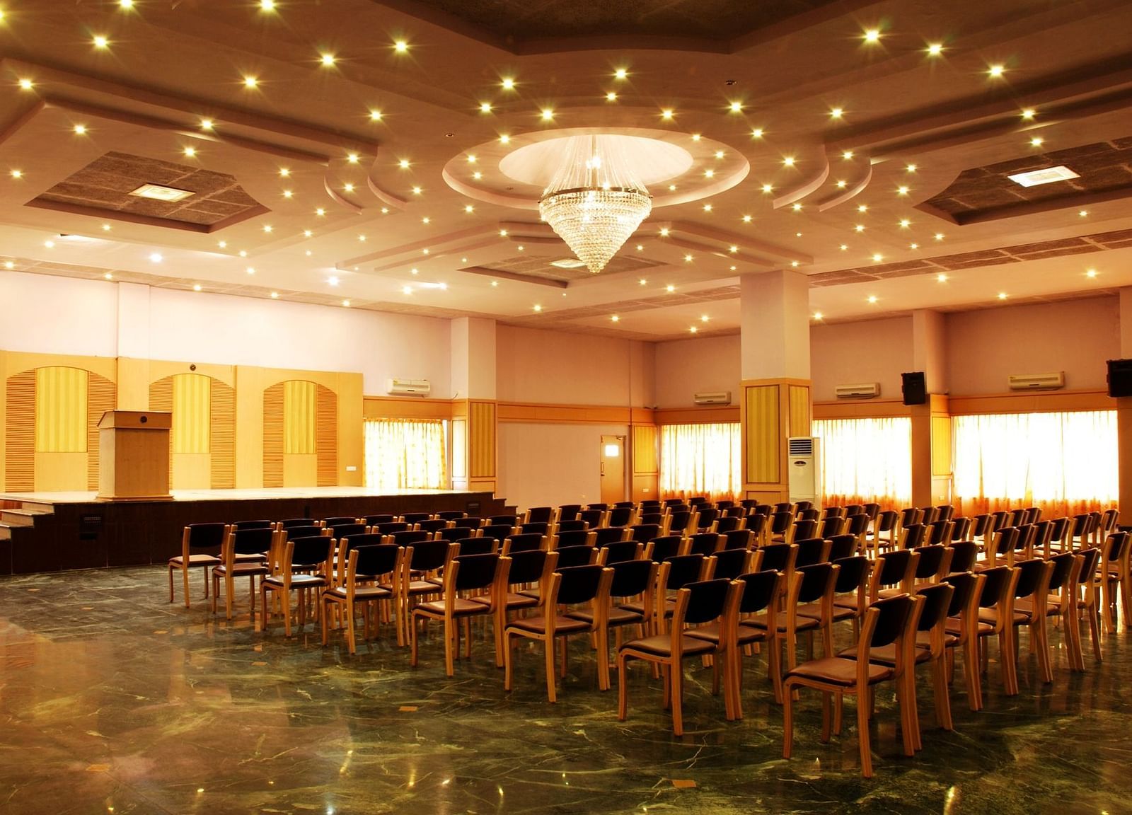 A view of a banquet hall at Paradise Isle Beach Resort, Udupi with a chandelier and a theatre style seating arrangement