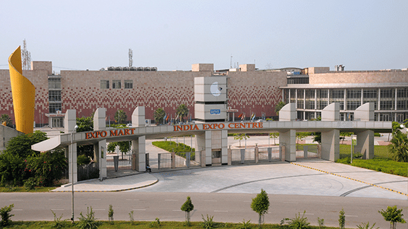 Wide exterior view of a large modern institutional building entrance with manicured lawns under a clear sky.