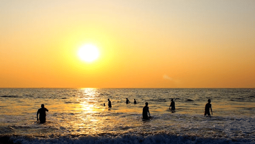 An ocean scene with individuals enjoying the water as the sun sets.