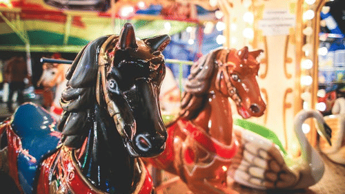 A close-up of carousel figures, including horses and a swan, at a fair.