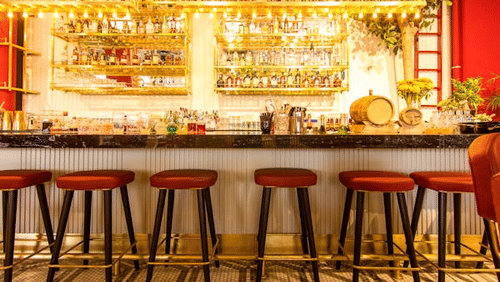 Brightly lit bar with high stools and a wide array of liquor bottles.