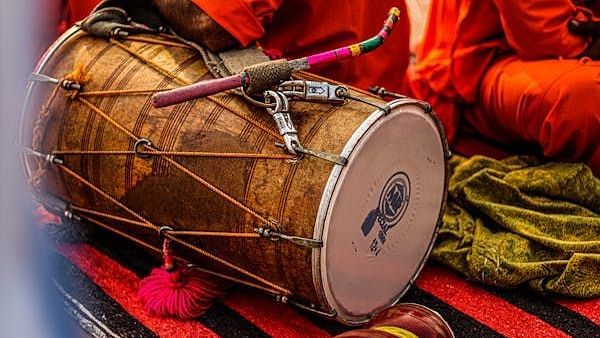 A traditional dhol drum with lacing and metal hardware, lying horizontally on a patterned cloth.