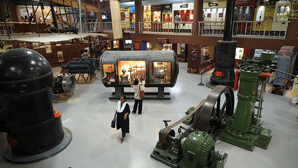 People view historical engineering inventions and vintage engine displays on the spacious main floor of Visvesvaraya Industrial and Technological Museum.