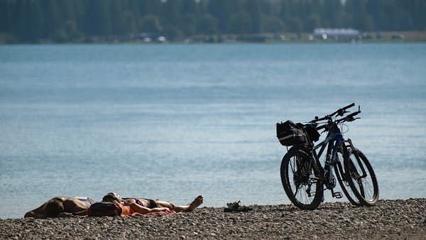 Two bikes stand on a pebbled shore beside a calm lake.