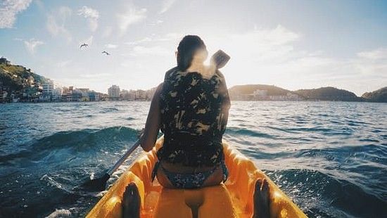 A shot taken from a kayak showing a person kayaking in rough waters, on a sunny day.