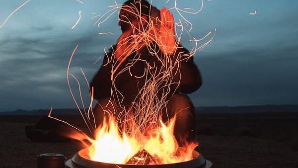 Image of a person warming themselves by a bonfire | Faraway Cottages, Auli