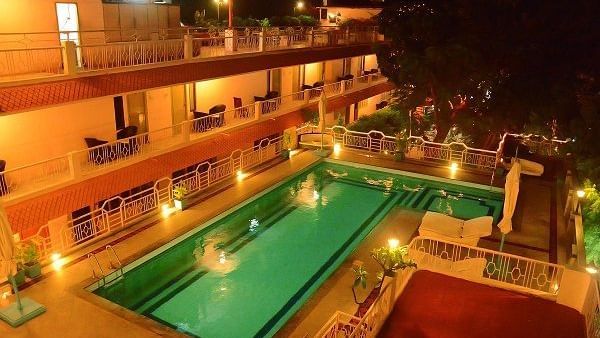A swimming pool with a lounge at poolside and surrounded by room balconies and lights in the evening at Hotel Mamallaa Heritage, Mahabalipuram.