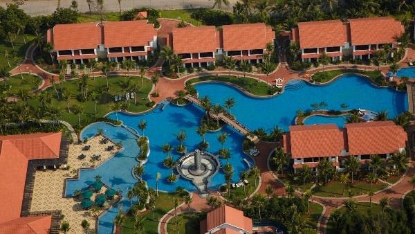 An aerial view of Hotel Mamallaa Heritage, Mahabalipuram, showing multiple red-roofed buildings, greenery, winding paths and pools.