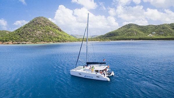 Boat sailing on clear blue waters near green hills.