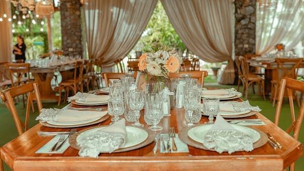 Banquet hall with wooden dining table filled with cutlery and plates and glasses.