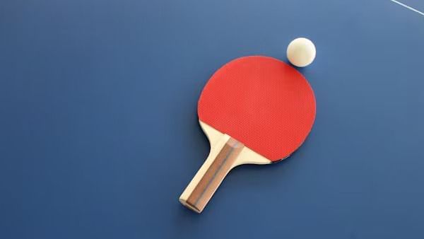 A table tennis paddle and ball resting on a table, with part of the boundary line visible in the corner.