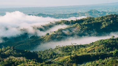 View of a misty valley with hills and a winding river below the clouds.