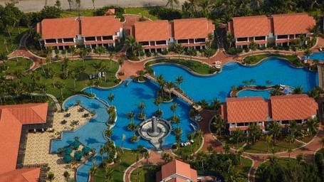 An aerial view of Hotel Mamallaa Heritage, Mahabalipuram, showing multiple red-roofed buildings, greenery, winding paths and pools.