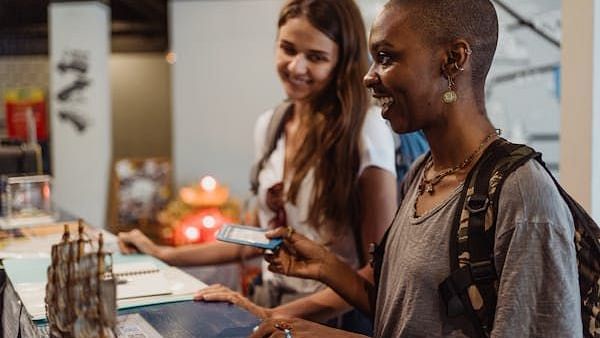 Two smiling young women at the reception desk are checking in with their phones.