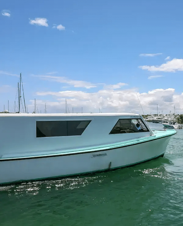 A white yacht anchored in a greenish-blue marina with a clear sky and distant shoreline visible.