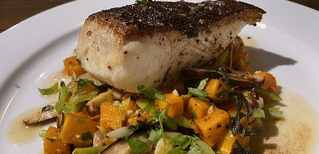 A seared piece of meat on a bed of roasted vegetables and a light sauce