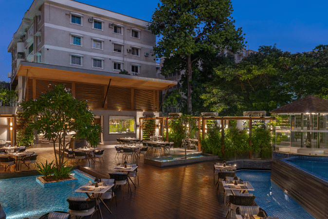 An outdoor swimming pool with a bar and lounge area, surrounded by lush greenery.