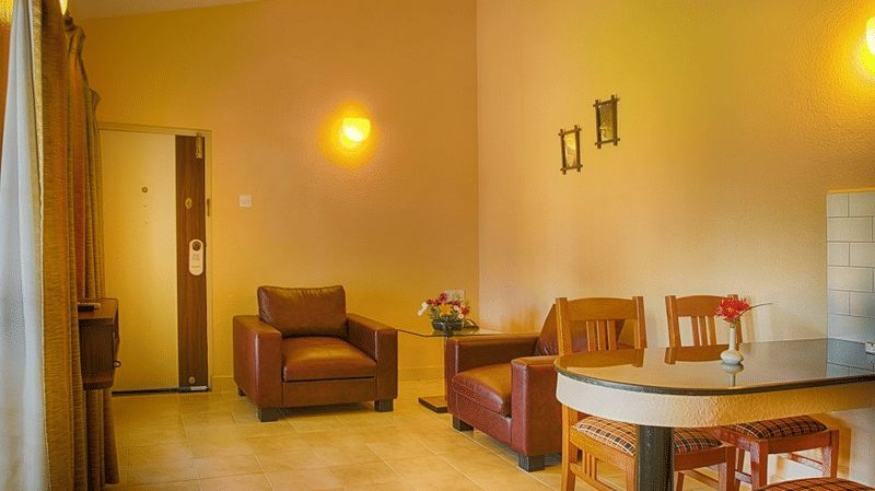 Room with a small sofa, two chairs, round dining table, beige walls, and a door leading to another area at Green Pastures, Kodaikanal.