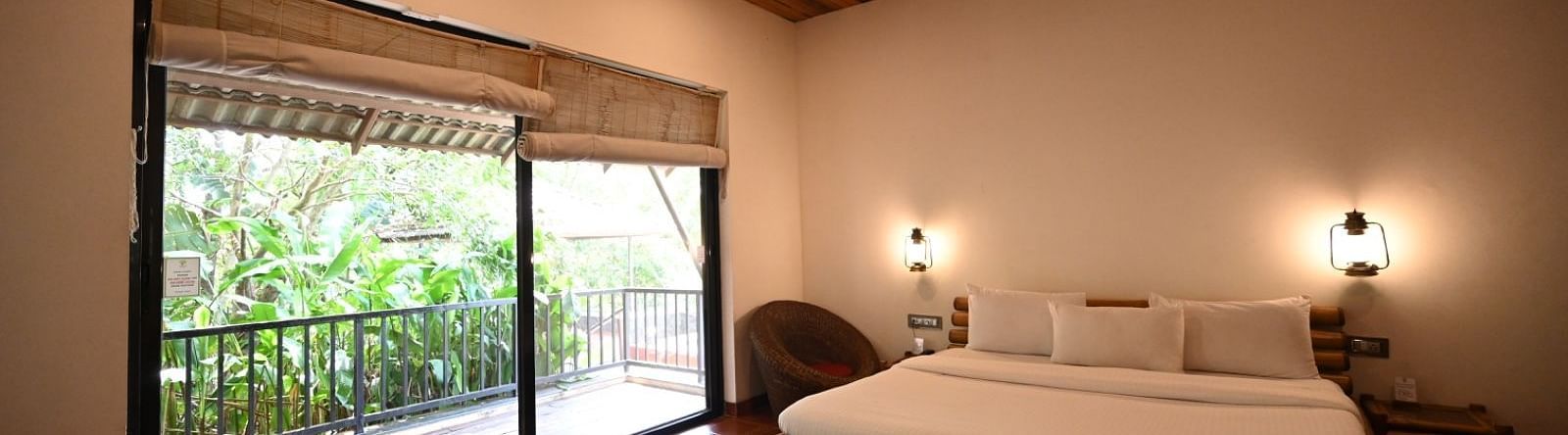 A bedroom with a wooden bed frame, white linens, and a window with a view of trees.