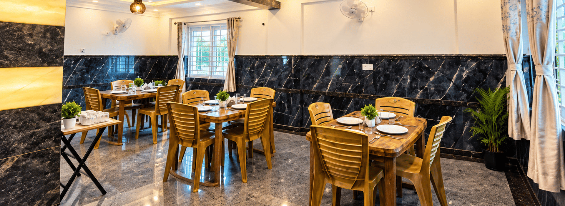 Dining area at Value Inn, Bangalore Airport with wooden tables and chairs set for a meal, black marble walls, curtained windows, and potted plants