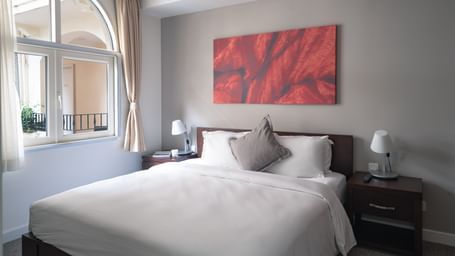 A bedroom with a large bed, a nightstand, and a piece of art on the wall | Two-bedroom Suite | Central Mansions, Phnom Penh
