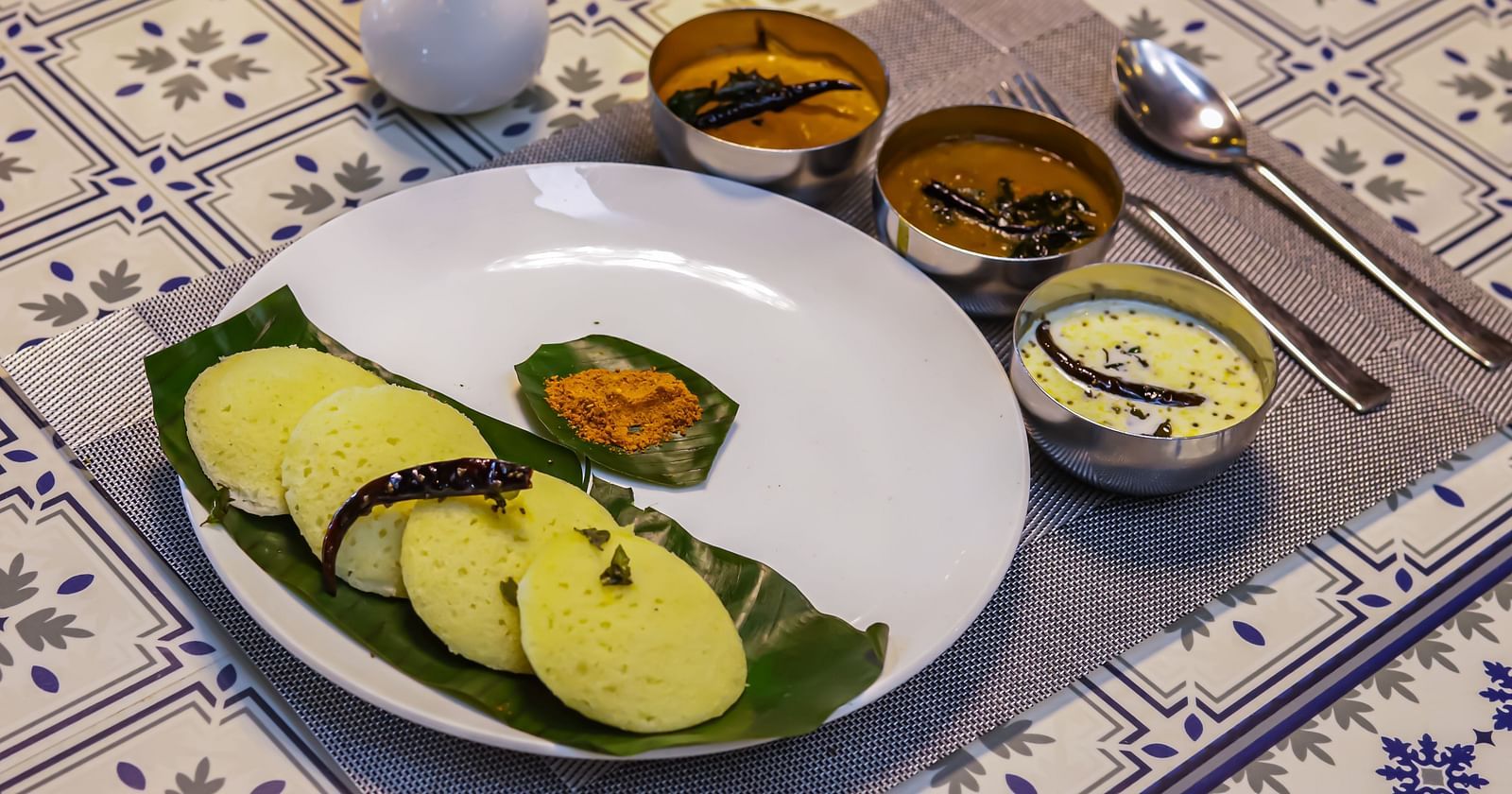 A white plate with food, accompanied by small bowls of sauces, rests on a patterned table at Vedikant Resorts The Mallard Corbett.