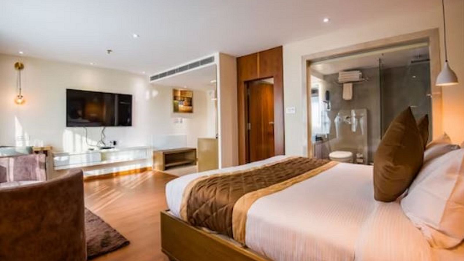 A premium hotel room with a large bed, a table to the side, a wall-mounted television, and a few fancy lamps around the room at Yashshree The Imperial Inn, Siliguri.