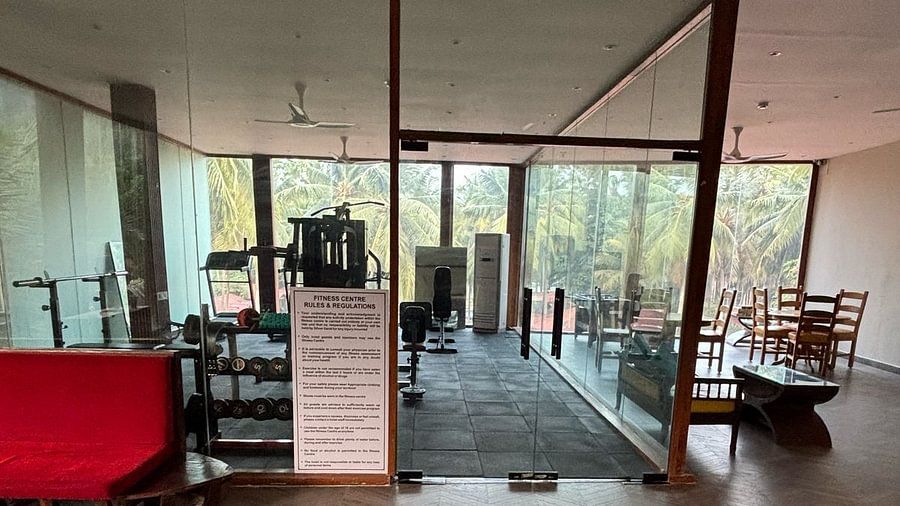 A modern gym entrance with wooden herringbone flooring, leading to a workout area with fitness equipment and large glass windows offering a view of greenery outside - Silver Sand Beach Resort, Havelock.