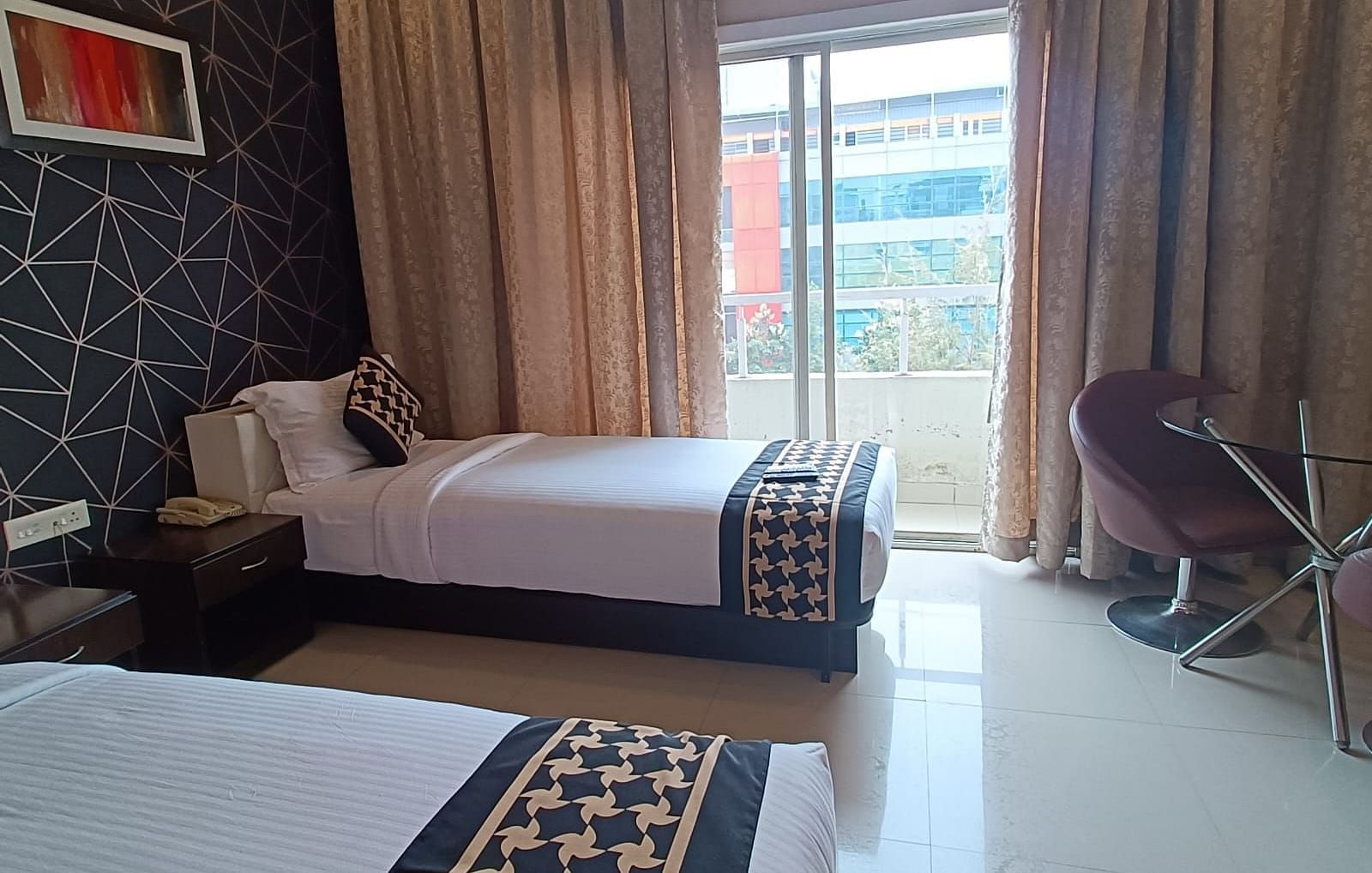 Hotel room designed for comfort and style, with two beds dressed in matching linens, a bold accent wall adding a touch of contemporary flair, and a huge glass window with an outdoor view, along with comfortable seating for relaxation - Astra Hotels & Suite
