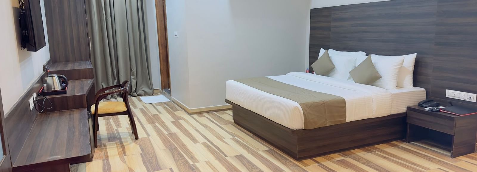 A room at Wild Wings Premium features a double bed with beige and white bedding, dark furniture, and wooden flooring - Kankidham Lords Inn