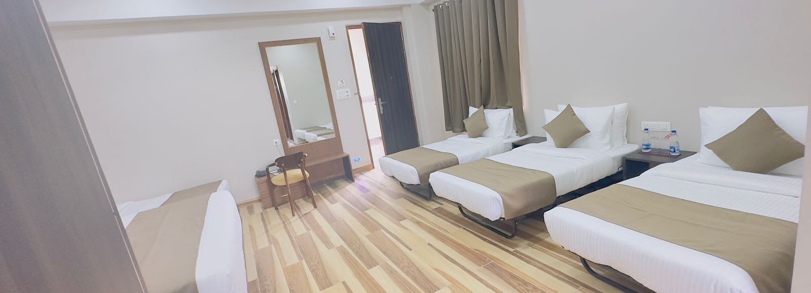 A spacious room features double beds with white and beige bedding, wooden floors, and ceiling fans - Kankidham Lords Inn