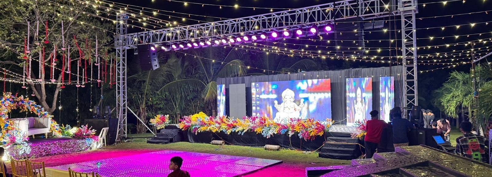 an outdoor event space with two stages, a well-lit decoration, and chairs arranged in a row with a complete audio visual system at Lords Hrim Akshara Resort, the best hotel in Basar, Telangana