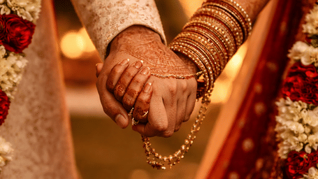 A close-up of a bride and groom holding hands during a wedding ceremony at Athiva Hotels & Resorts with traditional attire and floral garlands visible.