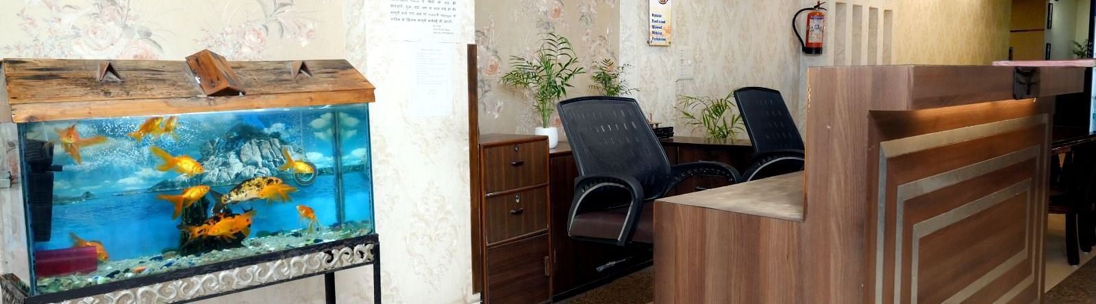 A hotel reception desk with a decorative fish tank, comfortable seating, and informative signs on the walls - Hotel Diamond Inn, Chandigarh