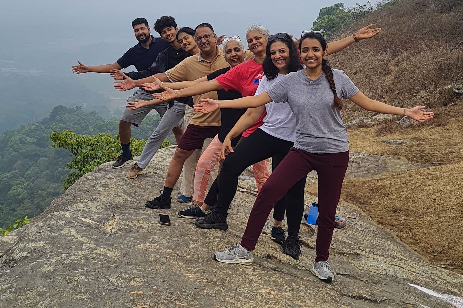 Group of people extending their arms joyfully on a mountain summit with a hazy background - Evergreen County