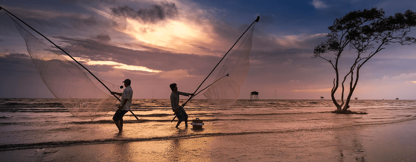 Two man casting out their net to fish by the seashore with the evening sky in view