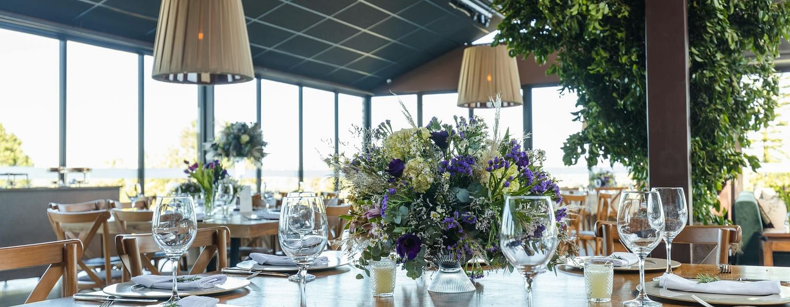 A banquet hall setting with round tables adorned with fine tableware and floral centrepieces under stylish lampshades.