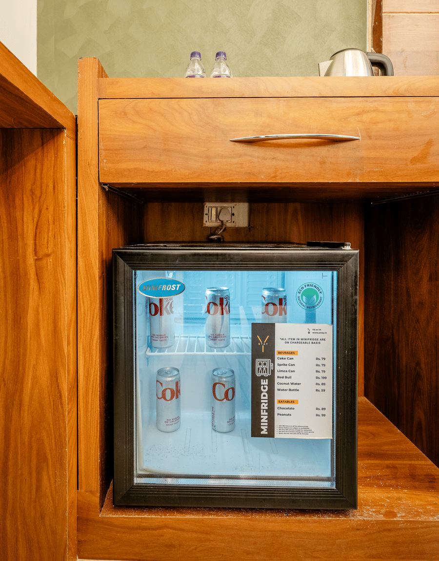 Compact black mini fridge stocked with beverages, built into a wooden hotel cabinet.