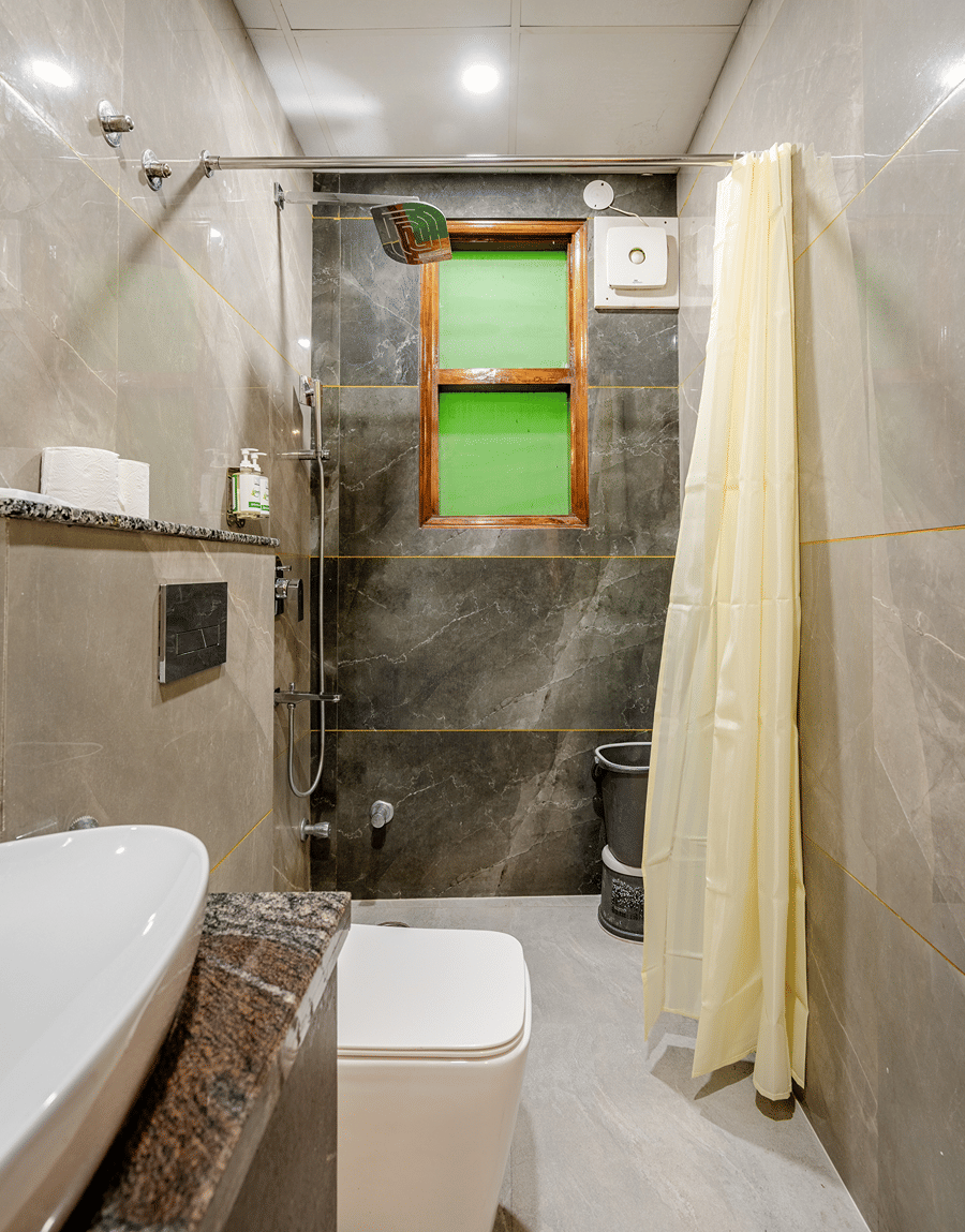 Bathroom with grey tiles, a shower curtain and a wall-hung toilet in the Deluxe Twin Room at Lime Tree Hotel Near Medanta