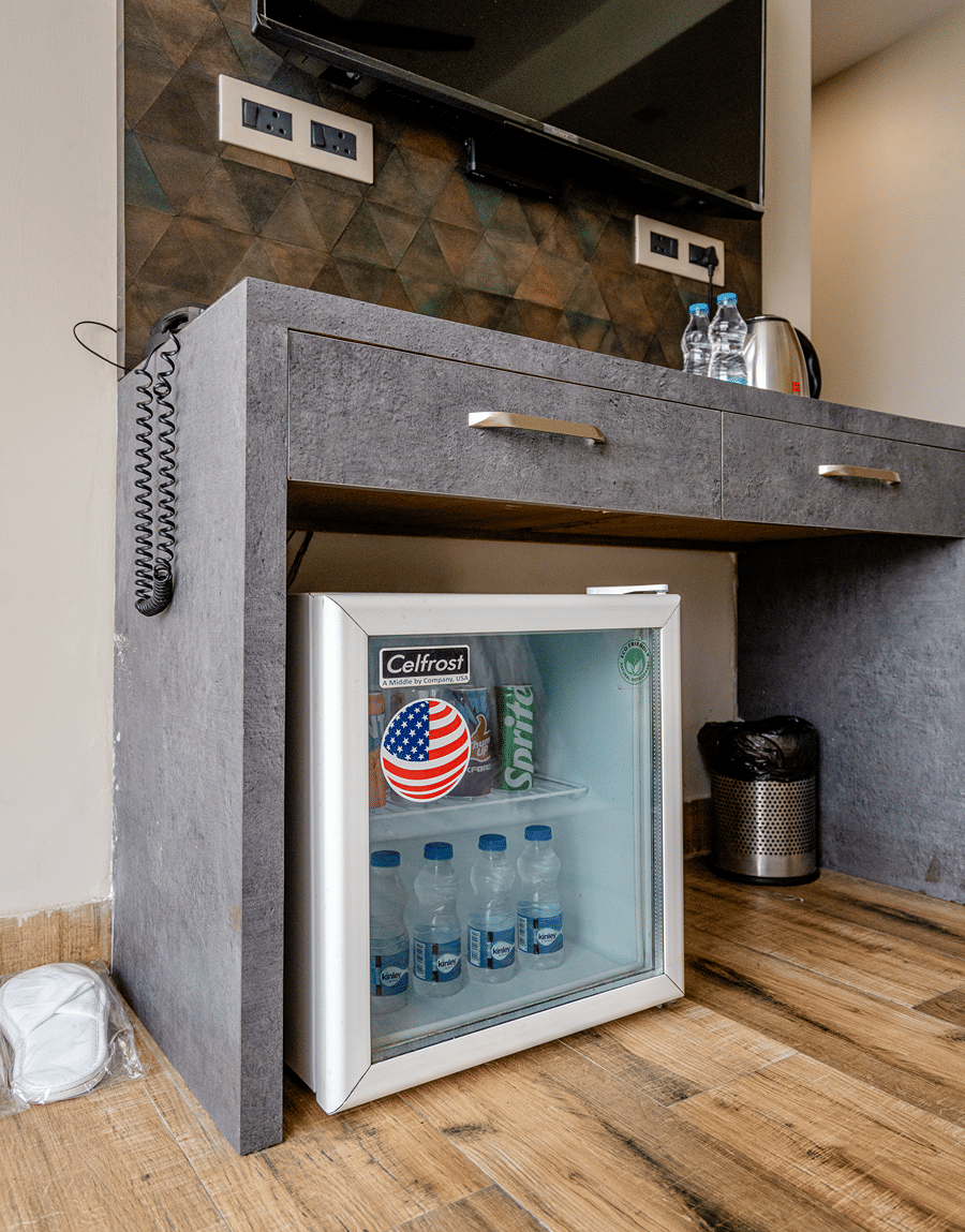 Glass-front minibar with water bottles below a console in the Deluxe Twin Room at Lime Tree Hotel Near Medanta