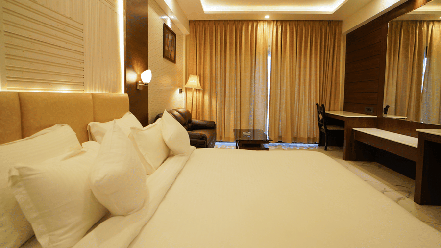 A neatly made bed with plush pillows in a bedroom at Shanti Seaview Resort & Spa, with a desk area and long window drapes.