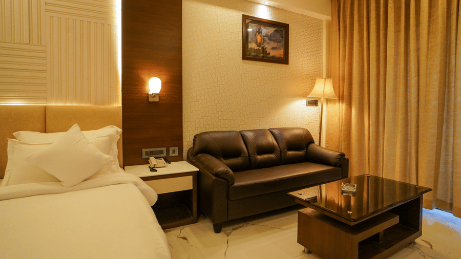 A bedroom featuring a seating area with a leather sofa and glass coffee table beside a neatly-made bed at Shanti Seaview Resort & Spa.