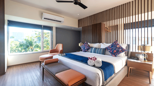 Studio Suite at Hotel Le Grande with a large bed, stylish décor, lounge chair by a sunny window, and contemporary wooden accents throughout.